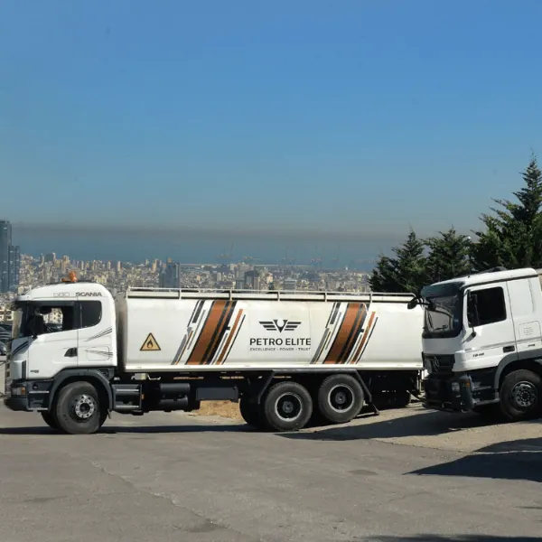 Two Petro Elite tanker trucks parked on a hillside above Beirut, with the city and its port behind